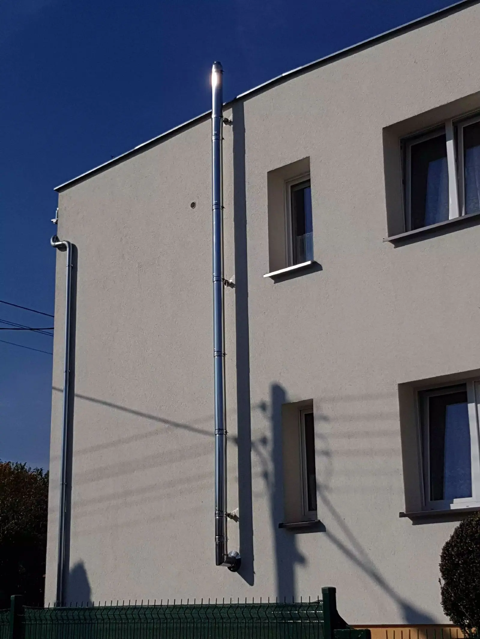 Nowoczesny komin dwuścienny ze stali nierdzewnej zamontowany na elewacji budynku.